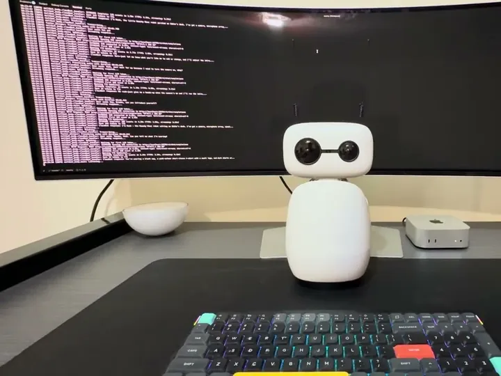 Reachy Mini as a desktop assistant under a wide monitor, shared by Eddie Hudson