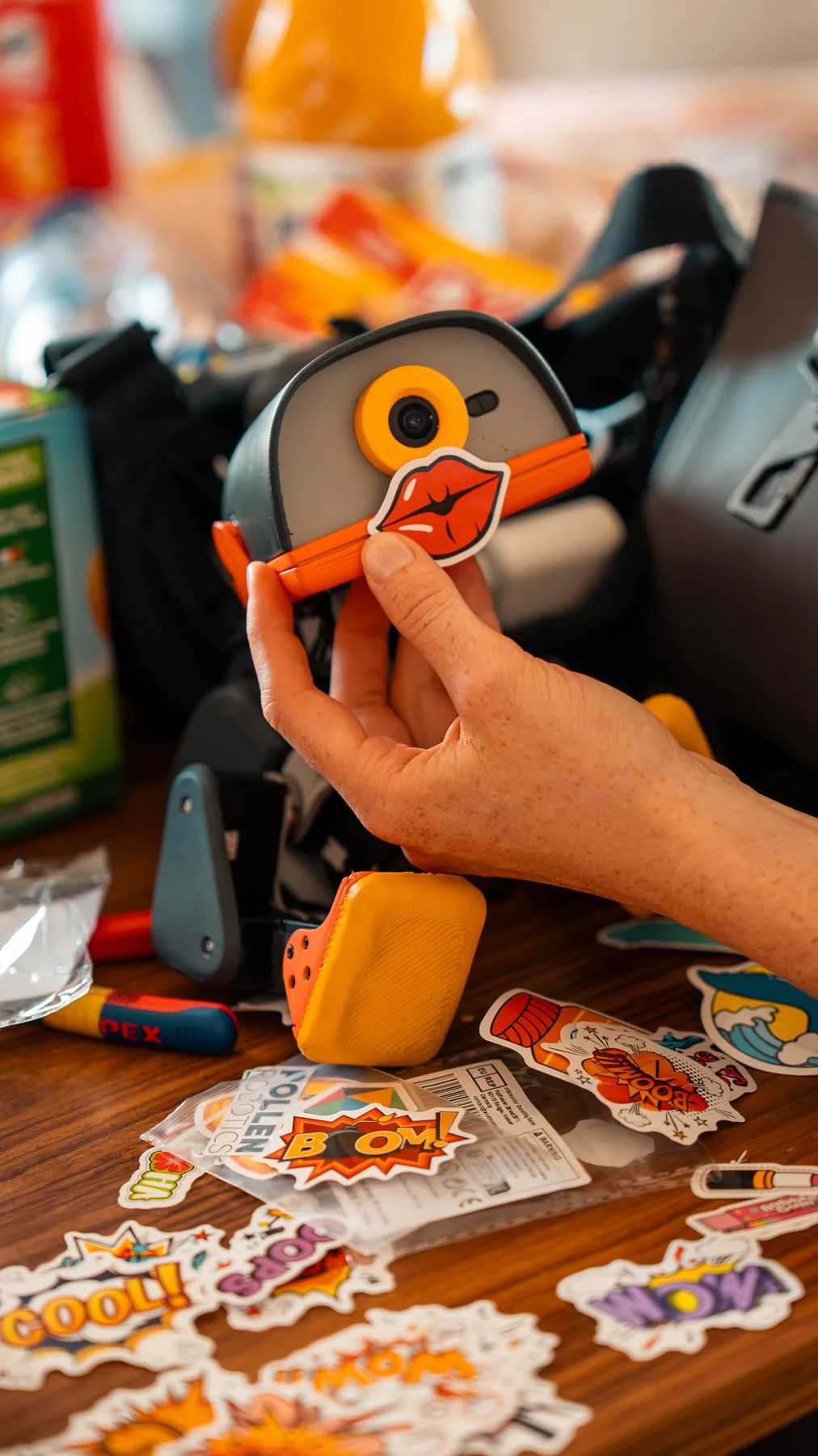 A hand sticking a lips sticker onto a Microduck's beak, sticker sheets spread on the table